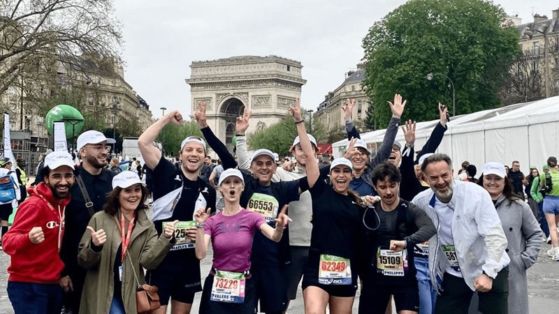 groupe de coureurs de Sanofi, après le Marathon de Paris, avec en fond d'image une vue sur l'Arc de Triomphe