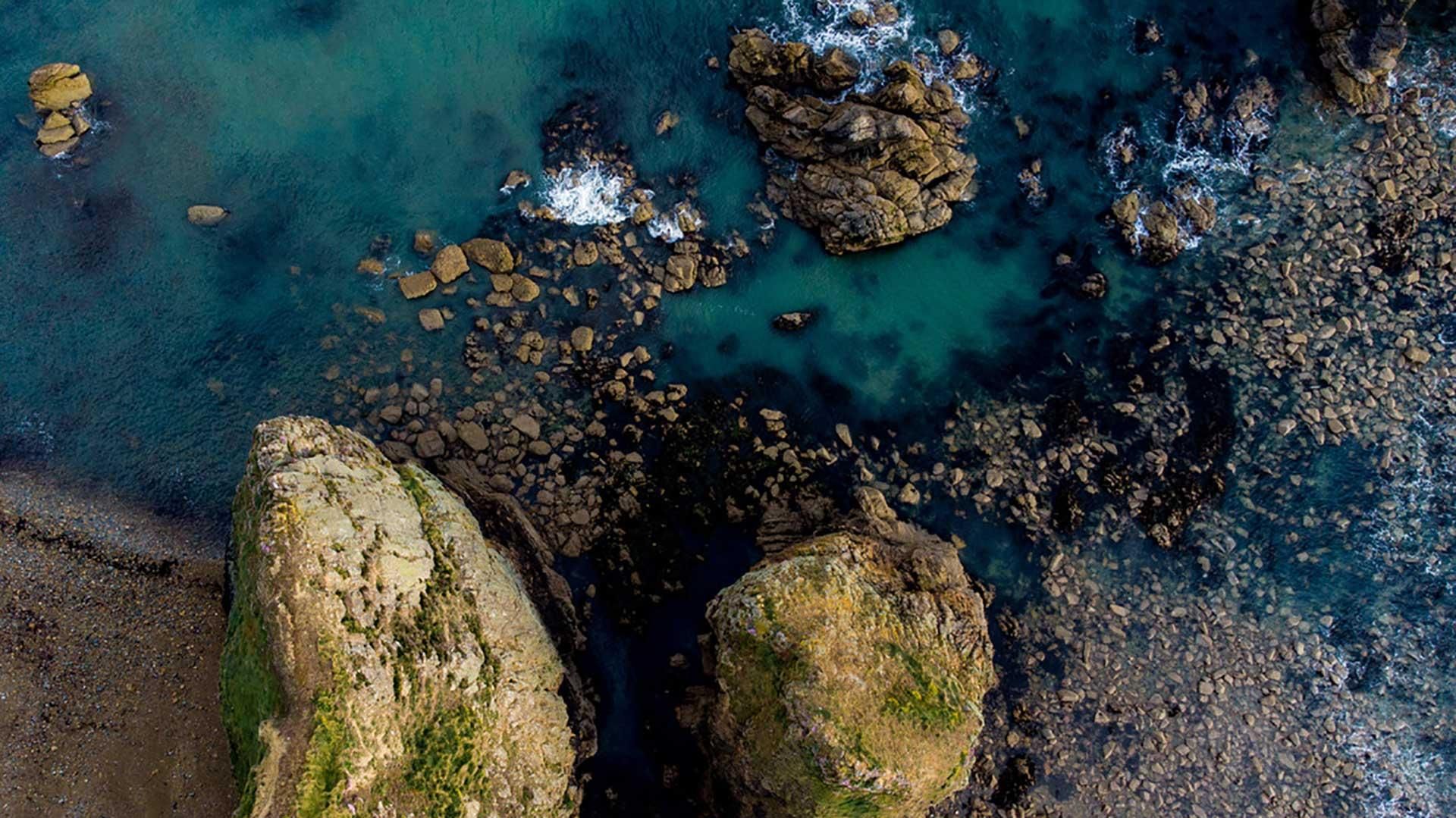 Vue aérienne d’une plage aux eaux turquoise et entourée de rochers.