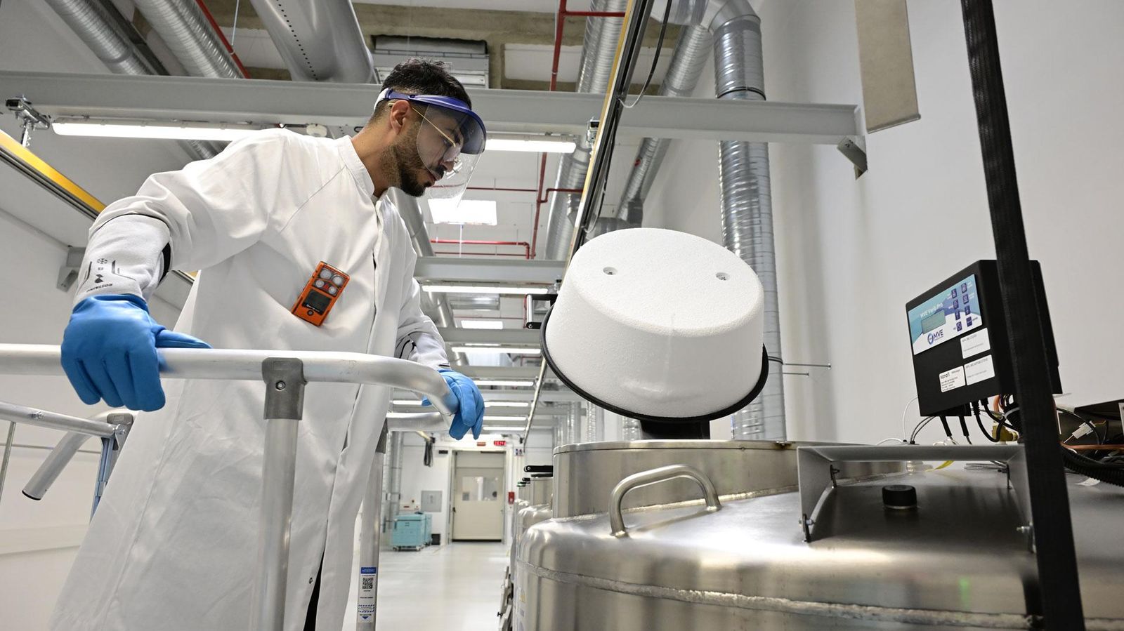Un technicien du Cryo Park de Sanofi, équipé de lunettes de protection, de gants et d'une blouse, se penche au-dessus d'une cuve en inox.