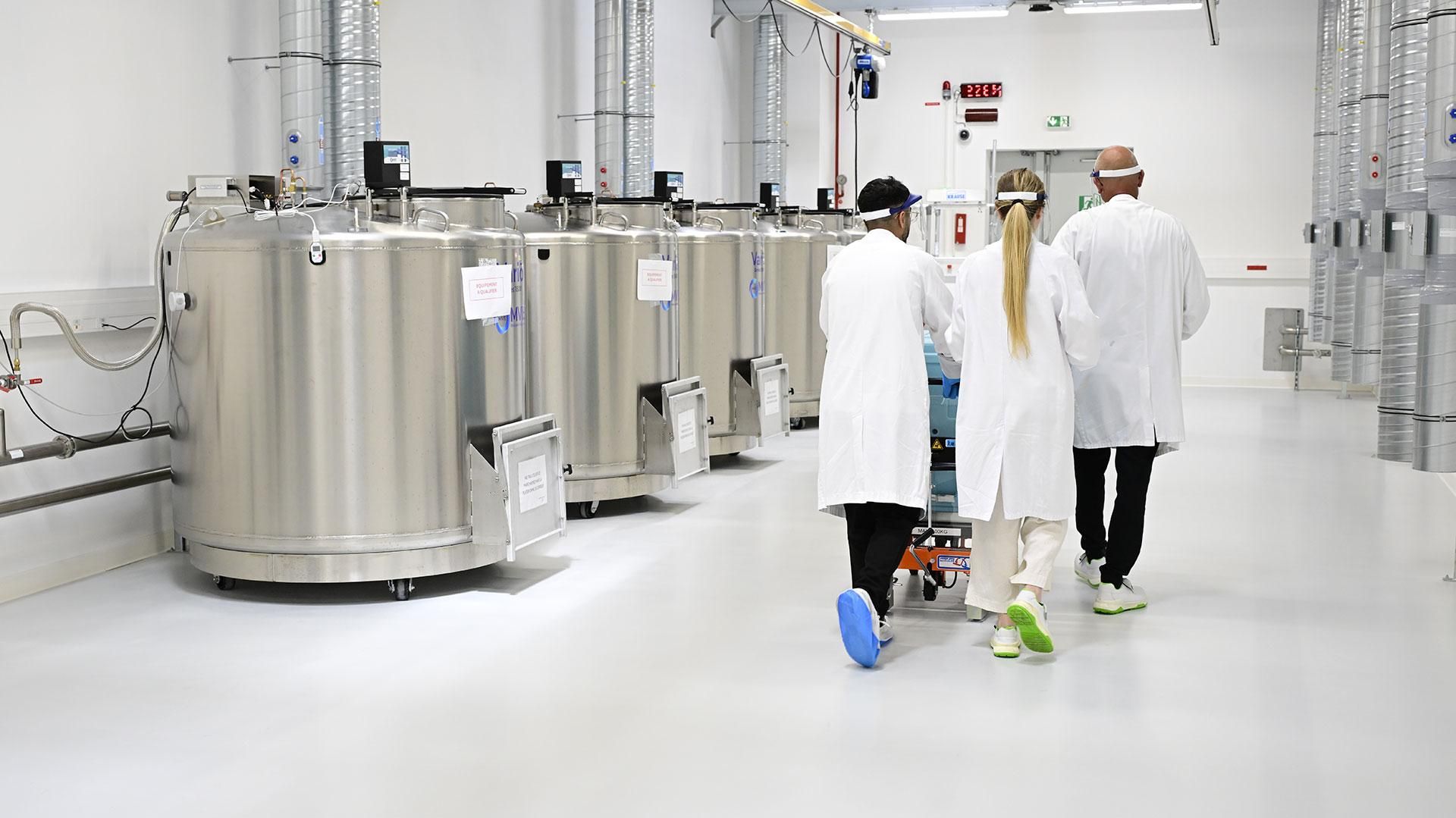 Trois opérateurs en blouses blanches et sur-chausses circulent à proximité des cuves de stockage grand froid du Cryo Park du site de Sanofi Montpellier.