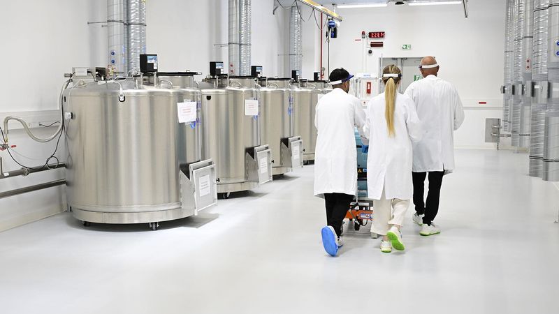 Trois opérateurs en blouses blanches et sur-chausses circulent à proximité des cuves de stockage grand froid du Cryo Park du site de Sanofi Montpellier.